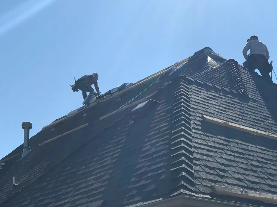 Superior Roofing crew working on a steep new charcoal shingle roof against a blue sky