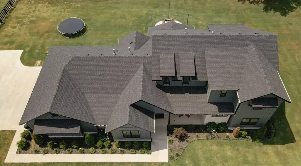 Drone view of a finished charcoal shingle roof with three dormers on a modern farmhouse in Northwest Arkansas