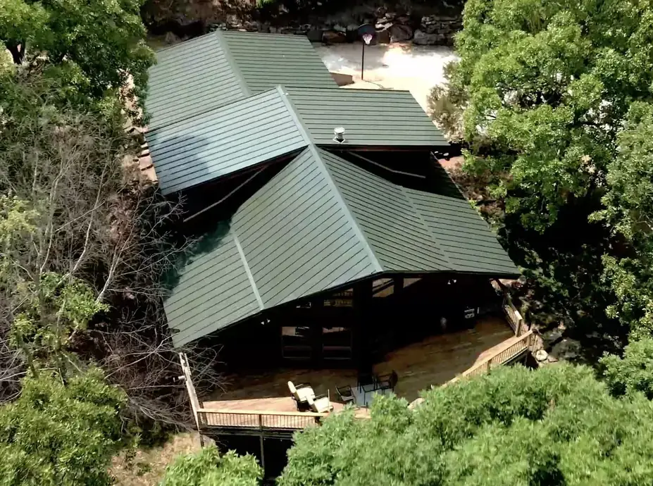Overhead drone view of a hunter-green metal roof on a wooded lodge-style home