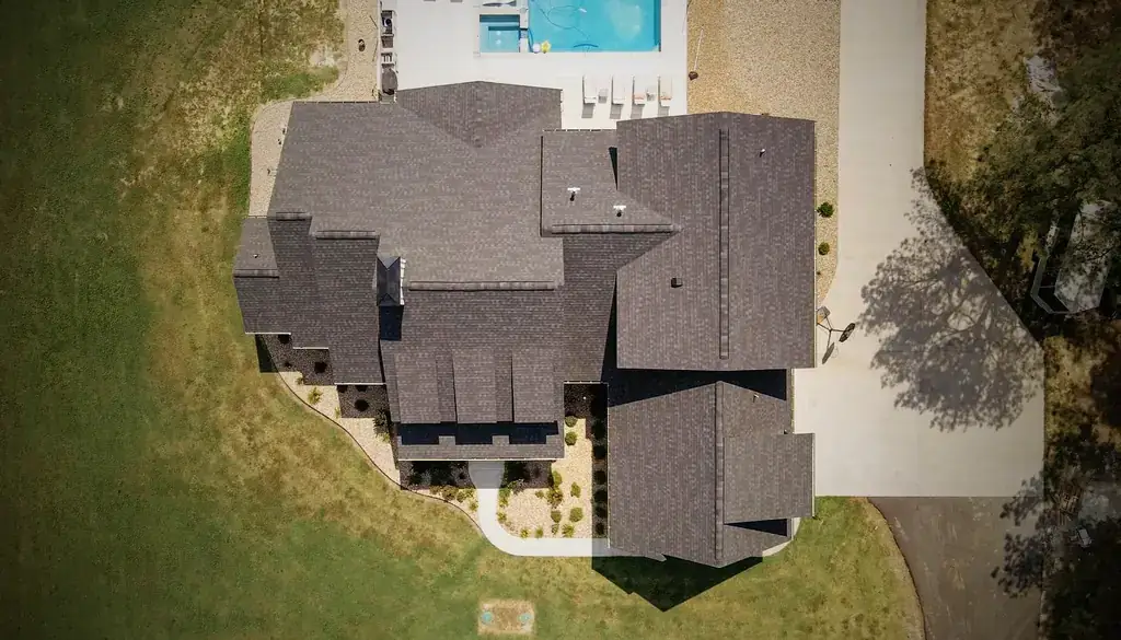 Straight-down drone view of a large finished charcoal shingle roof beside a pool, a Superior Roofing job